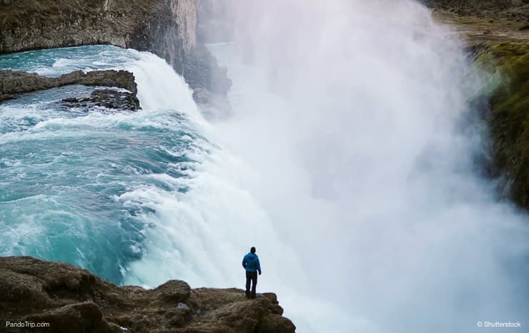 Hombre de pie en el borde de la montaña y mirando la cascada Gullfoss waterfall in Iceland