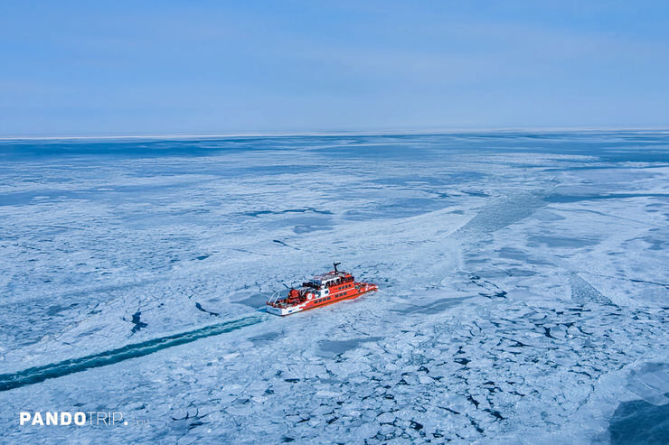 Garinko-go icebreaker ship navigating through a vast frozen sea, carving a clear path in the icy landscape under a bright blue sky