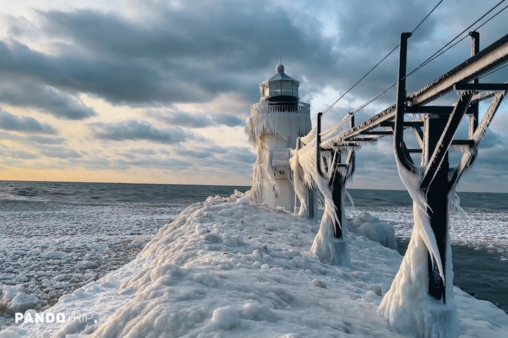 St. Joseph North Pier lighthouse coated in ice, icicle-draped steel catwalk, frozen Lake Michigan beneath dark winter clouds.