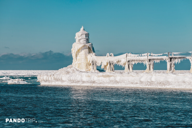 Surreal ice sculpture envelops St. Joseph North Pier outer lighthouse and icicle-draped catwalk on frozen Lake Michigan beneath a clear blue sky
