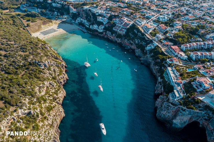 Aerial view of Cala en Porter bay with turquoise waters and cliffside village in Menorca, Spain