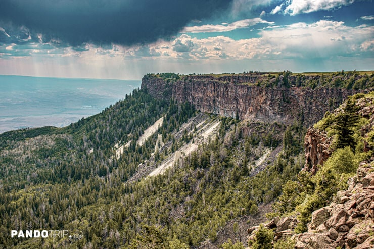 Vertical cliffs of Grand Mesa covered in dense forest beneath dark storm clouds