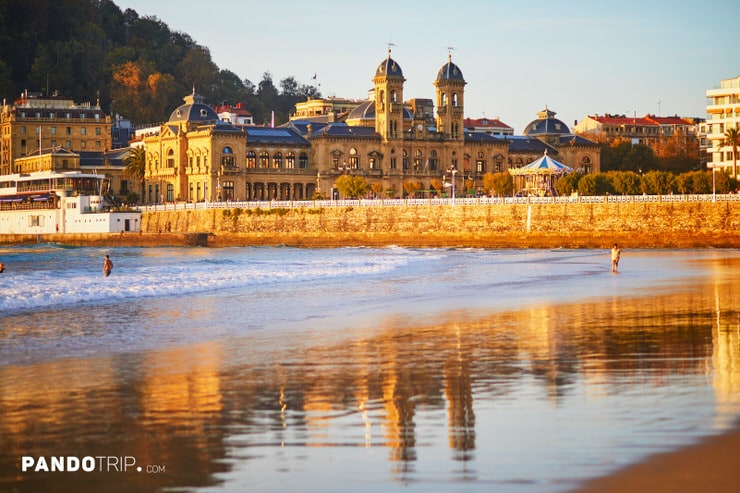 San Sebastián City Hall reflected in the wet sand near La Concha beach during sunset