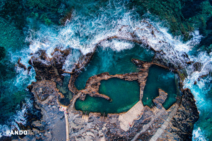 Aerial view of natural rock pools in Agaete with waves crashing on volcanic coastline