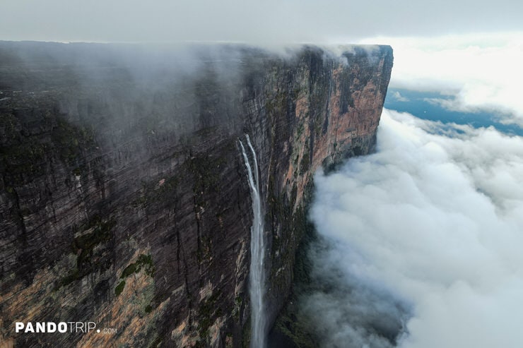 Aerial view of waterfalls flowing from Mount Roraima’s cliff face into dense clouds below