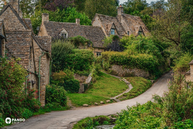 Elevated view of Arlington Row cottages and winding lane in Bibury village surrounded by summer greenery