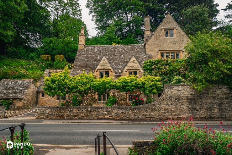 Stone cottage covered in roses and ivy beside the main road in Bibury village