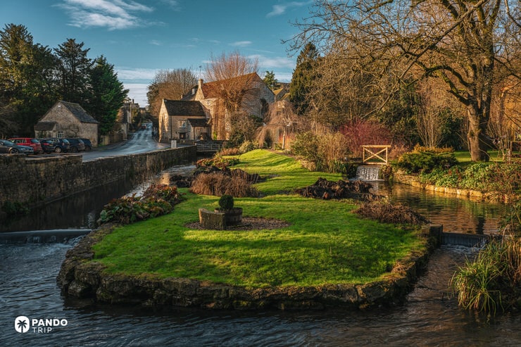 Small grassy island and weir on the River Coln near Arlington Mill in Bibury