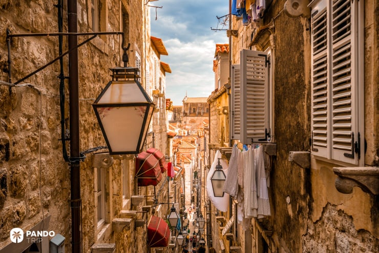 Steep, narrow stone alley in Dubrovnik with hanging lanterns, windows, and laundry lines