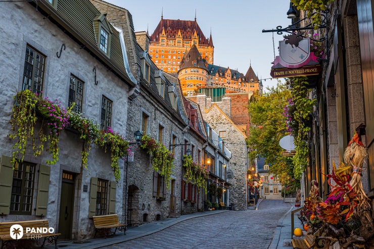 Cobblestone street in Old Quebec with flower-adorned houses and Château Frontenac rising in the background