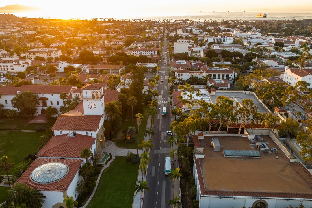 Aerial view of downtown Santa Barbara looking down Anacapa Street towards the ocean at sunset, featuring red tiled roofs.