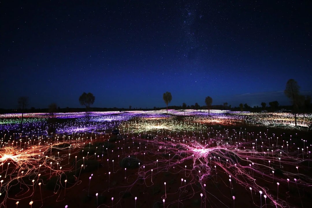 Bruce Munro’s Field of Light installation near Uluru, thousands of coloured light spheres glowing across the desert under a clear starry sky in Uluru-Kata Tjuta National Park, Australia.
