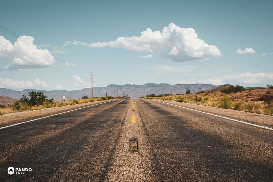 Low angle view along Route 66 showing the worn asphalt, yellow center line, distant mountains and big sky in rural American Southwest.