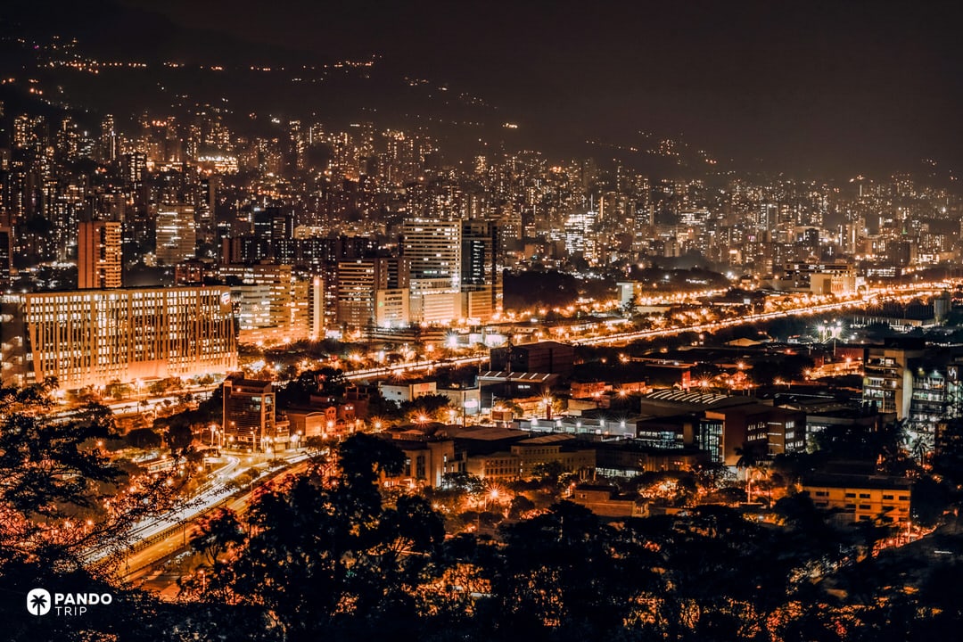 Night view over Medellín, Colombia, showing illuminated high-rise buildings and highways running through the Aburrá Valley.