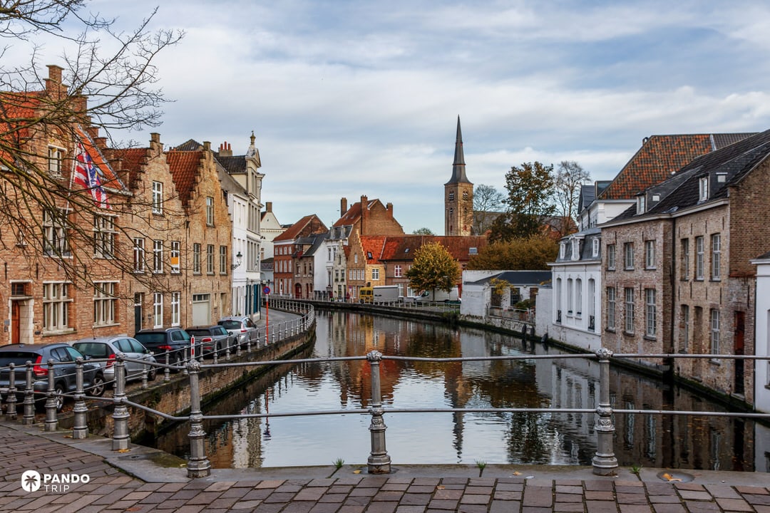 Peaceful Bruges canal lined with brick houses and a distant church spire