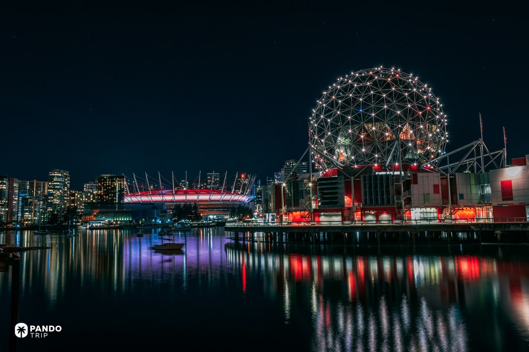 Night view across False Creek in Vancouver, with Science World’s illuminated geodesic dome, BC Place stadium and city skyline reflected in the water in British Columbia, Canada.