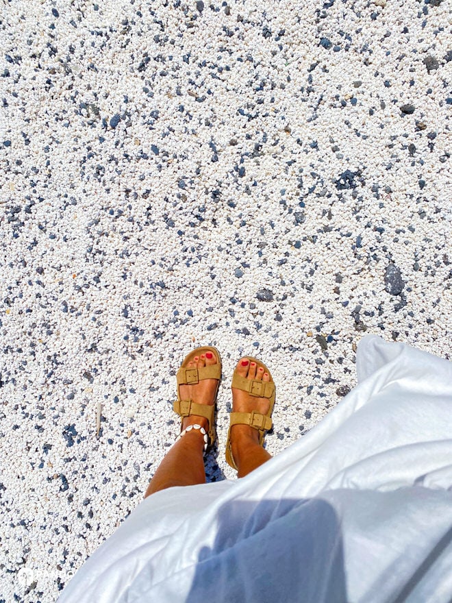 Top-down of sandals on Popcorn Beach’s white rhodolith carpet dotted with dark lava pebbles, Fuerteventura.
