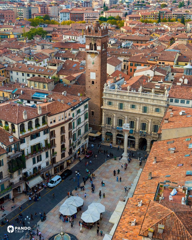 High-angle aerial shot of Verona showing the Torre dei Lamberti rising above the red rooftops and the market stalls of Piazza delle Erbe below.