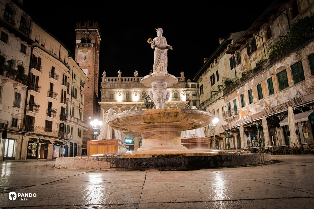 The Madonna Verona fountain statue illuminated at night in a dark, empty square, featuring a Roman-era female figure holding a scroll.