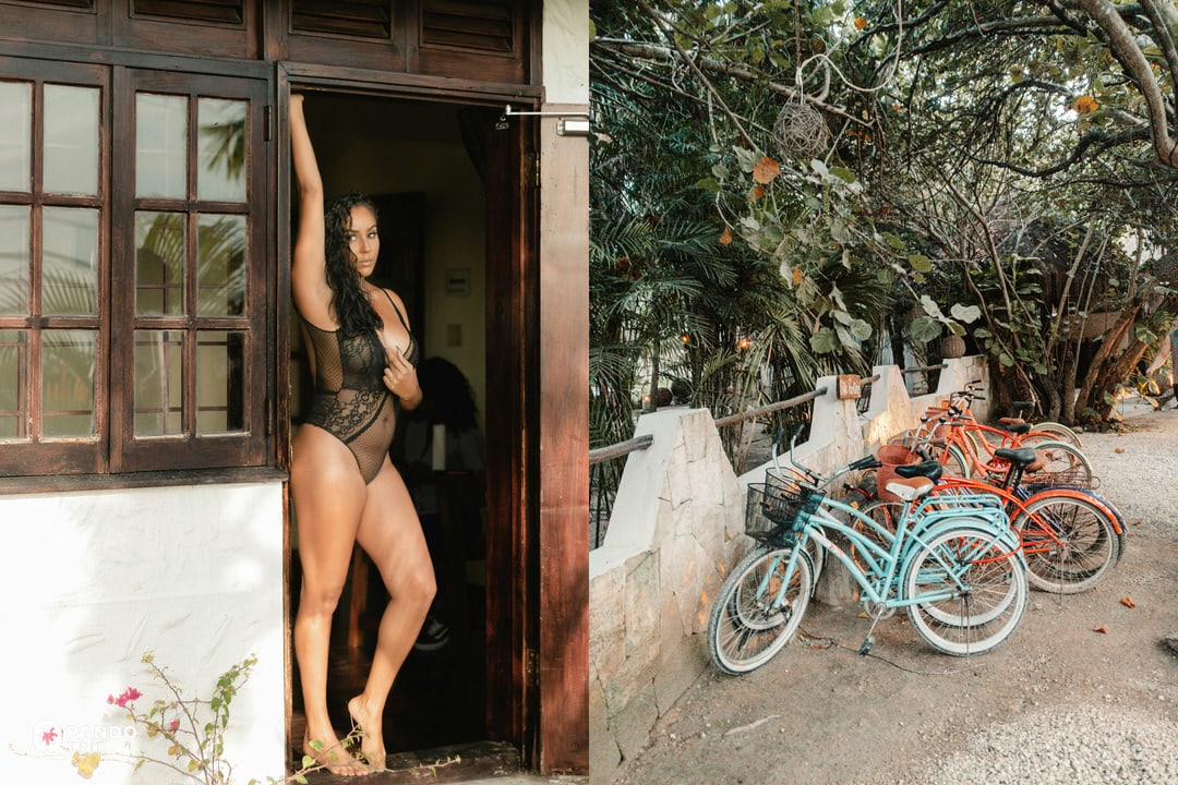 Woman wearing a black sheer bodysuit standing in a rustic doorway, next to a row of colorful bicycles parked in a tropical Tulum setting.