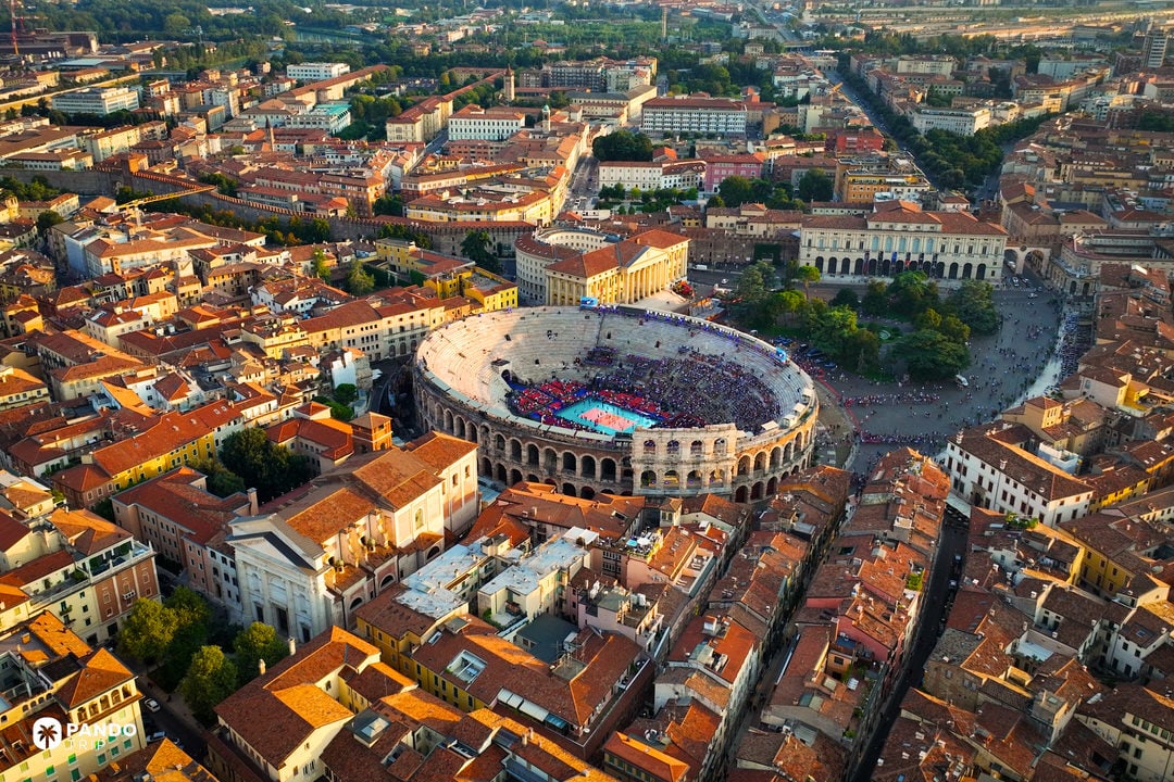 Aerial view of the Verona Arena and Piazza Bra during golden hour, showing the massive elliptical Roman amphitheater surrounded by the city.