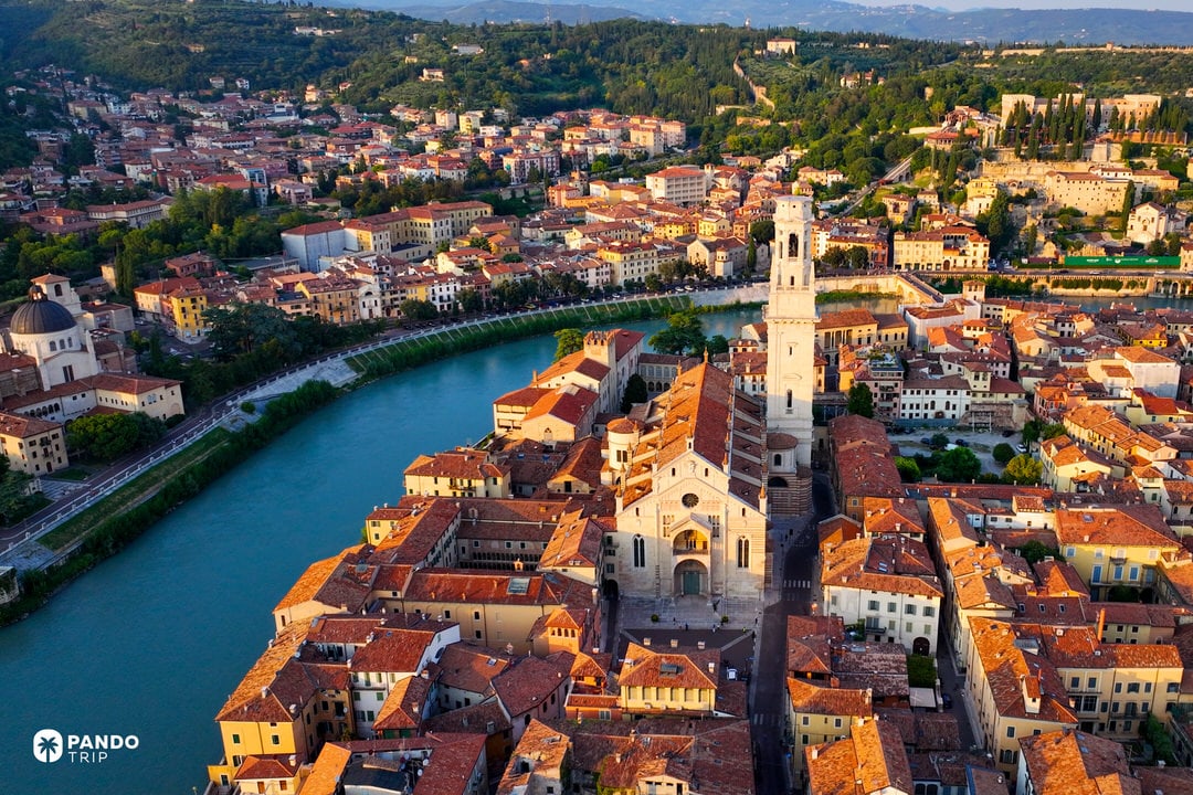 Aerial view of Verona at golden hour, showing the Adige River curving around the historic center and the Verona Cathedral bathed in warm sunset light.