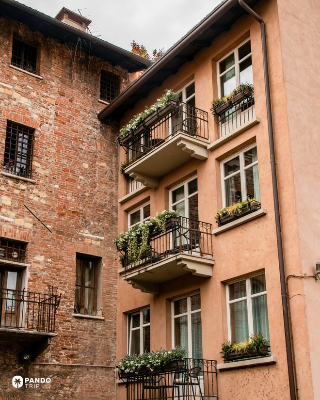 A facade of a historic terracotta-colored building in Verona featuring multiple iron balconies with flower boxes.
