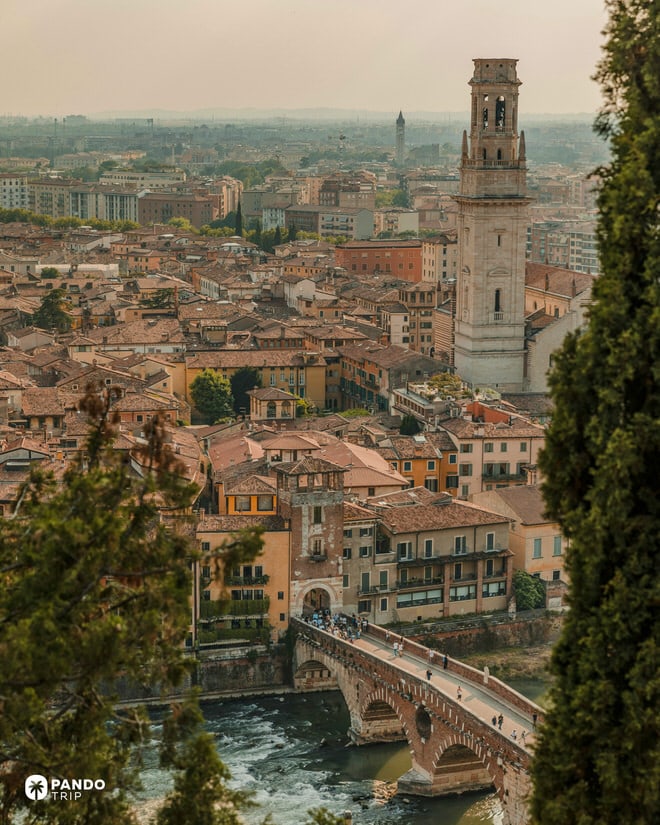 High-angle view of Verona skyline featuring the Torre dei Lamberti and Ponte Pietra bridge over the Adige River at sunset.
