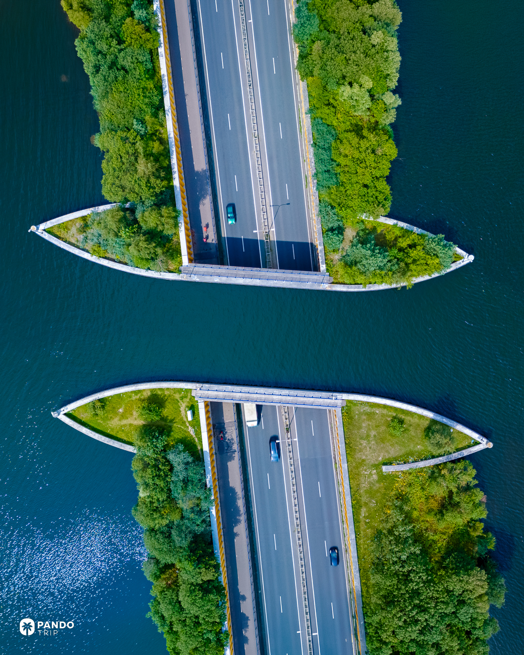 Overhead view of the Aquaduct Veluwemeer showing both carriageways of the N302 and the separate cycle path, with the empty water channel between the tree-covered banks.