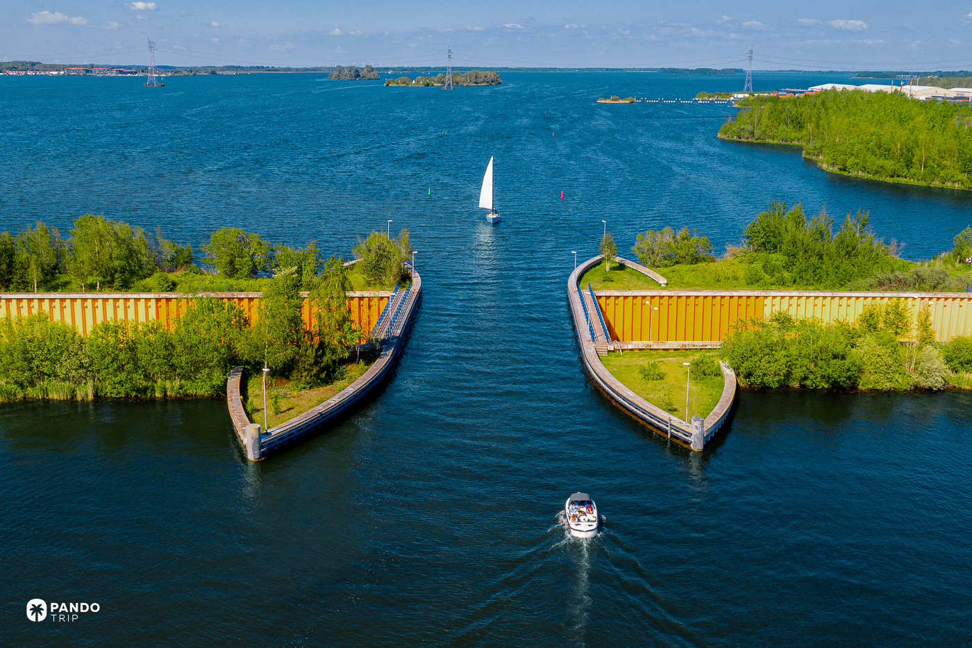 Low view along the water channel of the Aquaduct Veluwemeer, a motorboat approaching and a sailing yacht beyond, the orange walls of the N302 on either side.