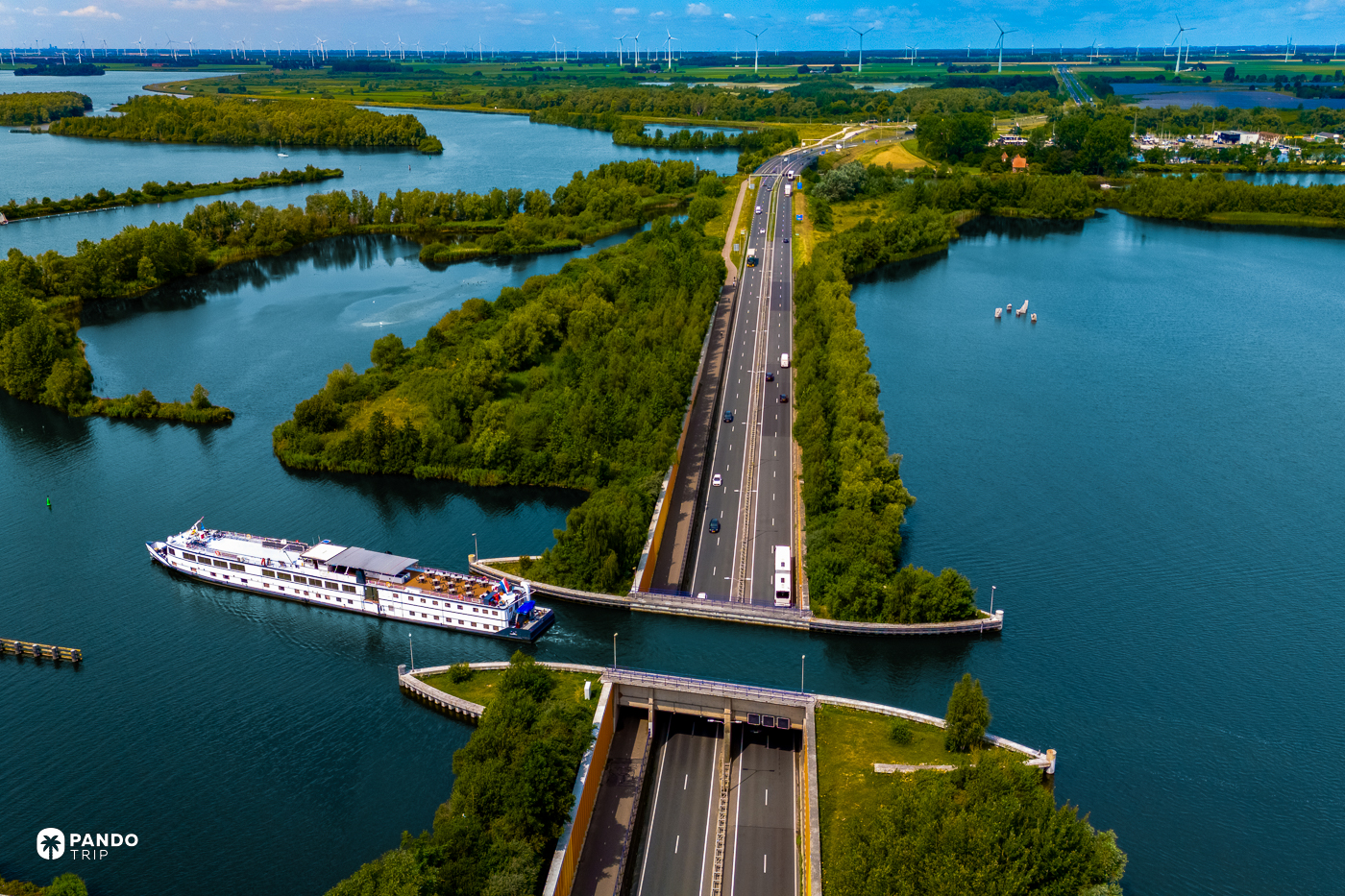 A white passenger ship crossing the Aquaduct Veluwemeer above the N302, traffic running along the sunken road toward the tunnel mouth below.