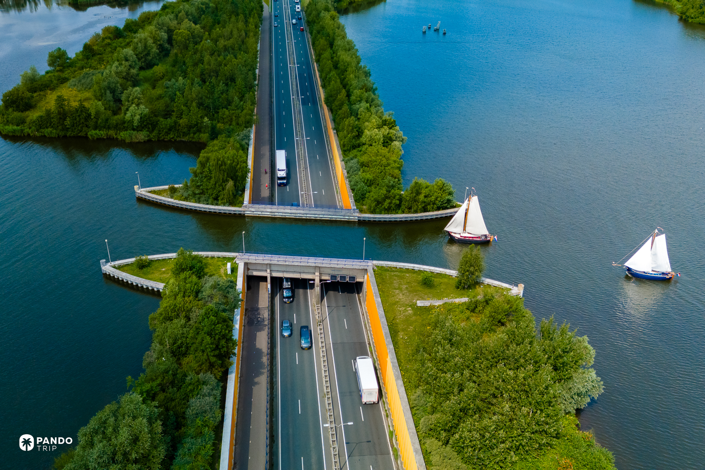 Two traditional flat-bottomed sailing barges on the Veluwemeer beside the aqueduct, a truck and cars on the N302 dropping into the tunnel beneath the water.