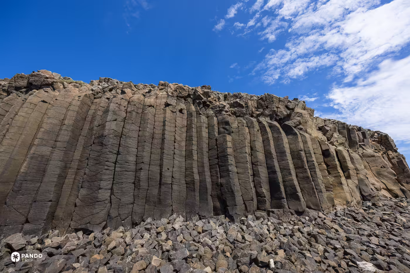 Weathered basalt columns rising in a wall above loose scree under a blue sky in Penghu.