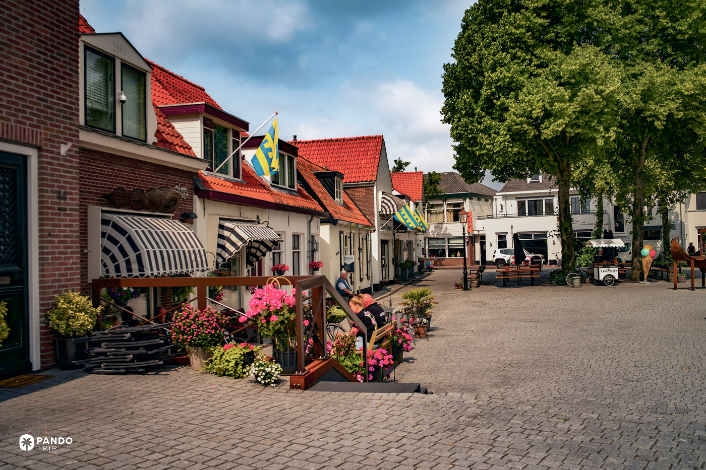 Cobbled square in the old town of Harderwijk, brick and white-painted houses with striped awnings, flowers and Gelderland flags.