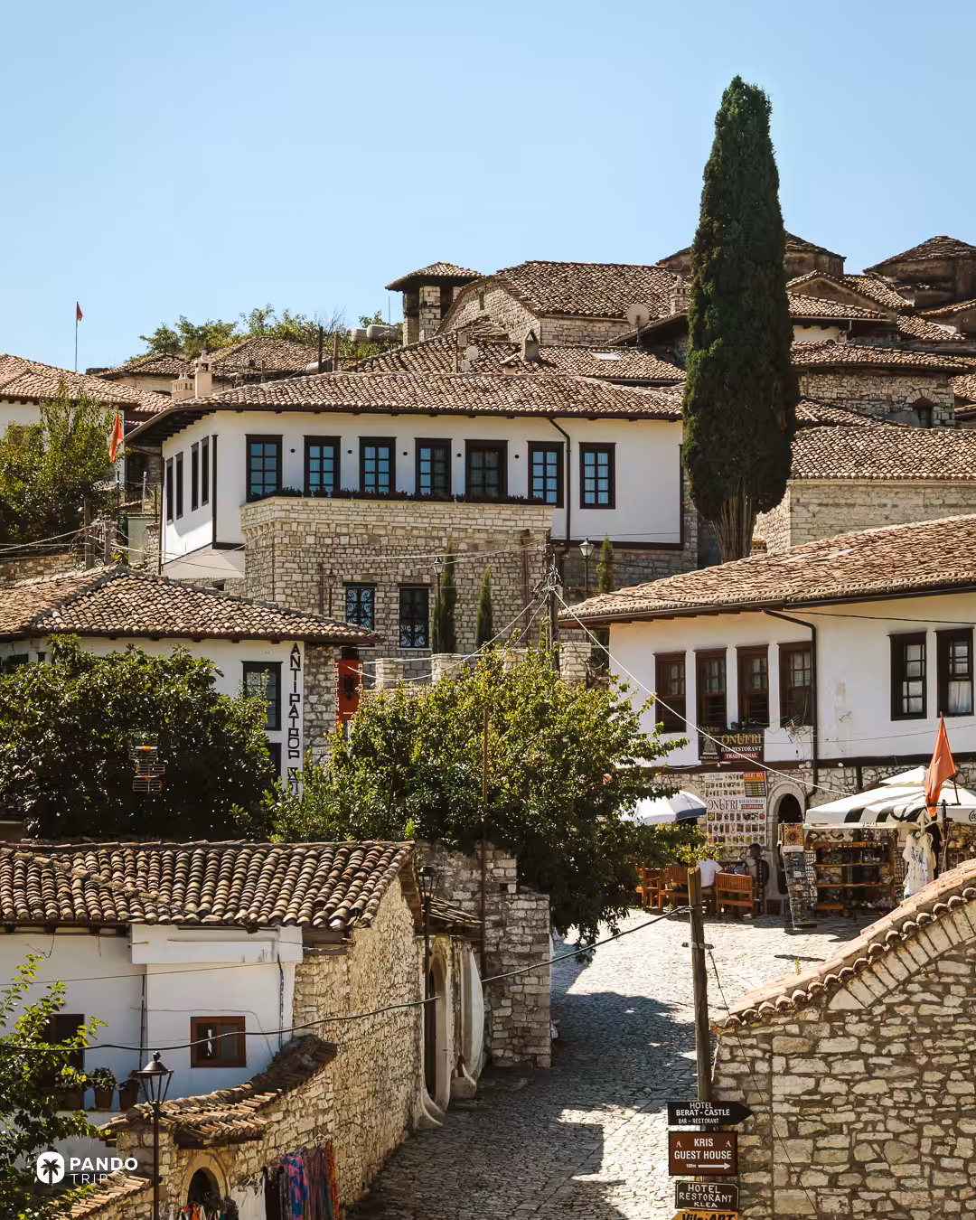 A cobbled lane between stone houses inside Berat's castle walls, guesthouse and restaurant signs at the corner.