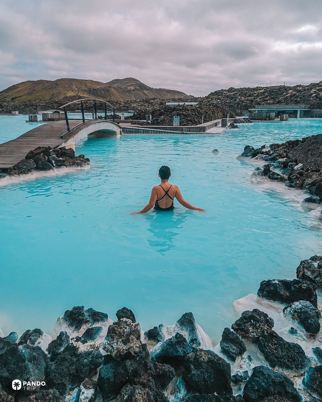 A bather in the milky blue water of the Blue Lagoon on Iceland's Reykjanes peninsula, black lava banked around the pool.