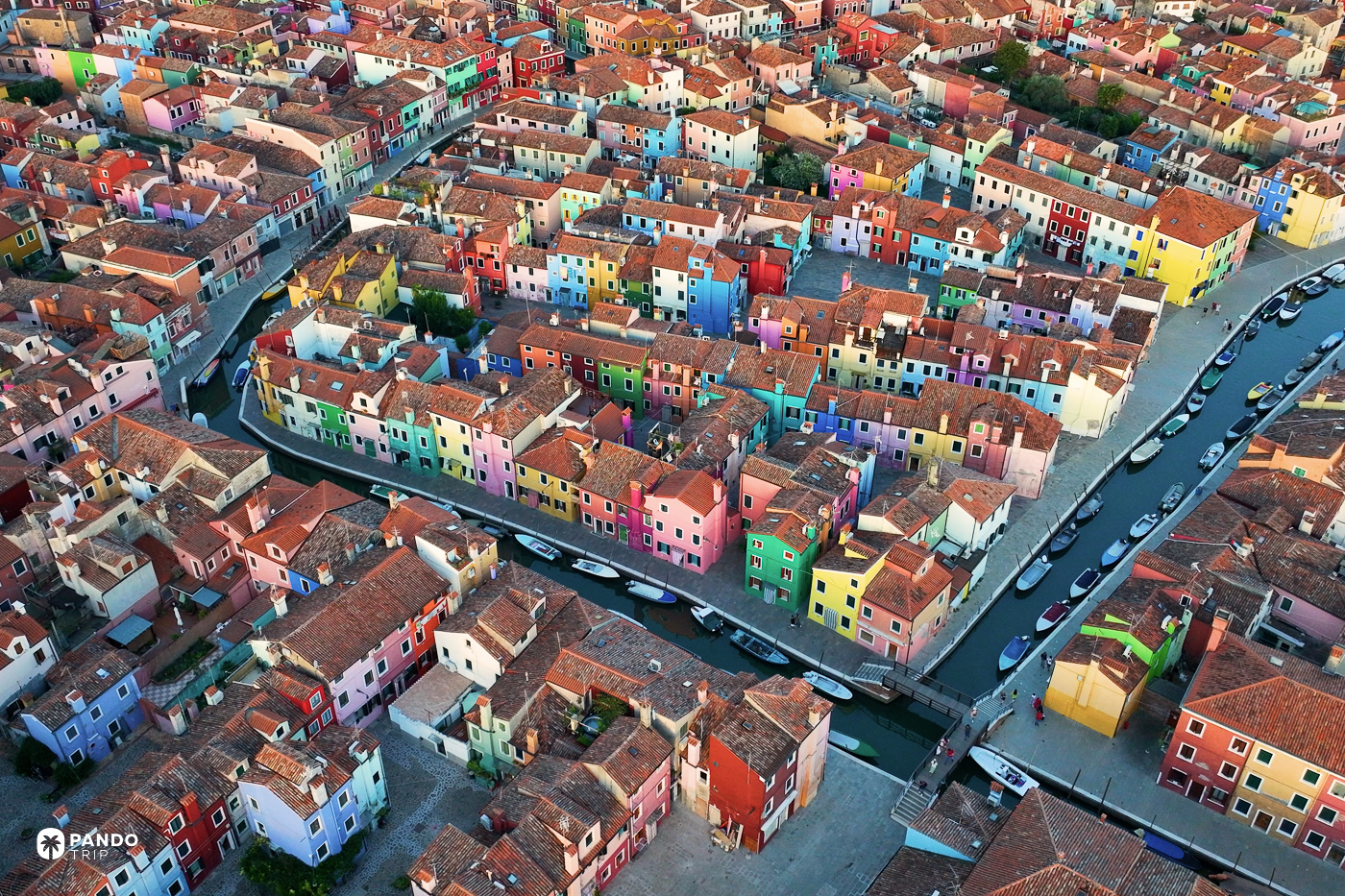 Rows of brightly painted houses along a canal on Burano, seen from above.