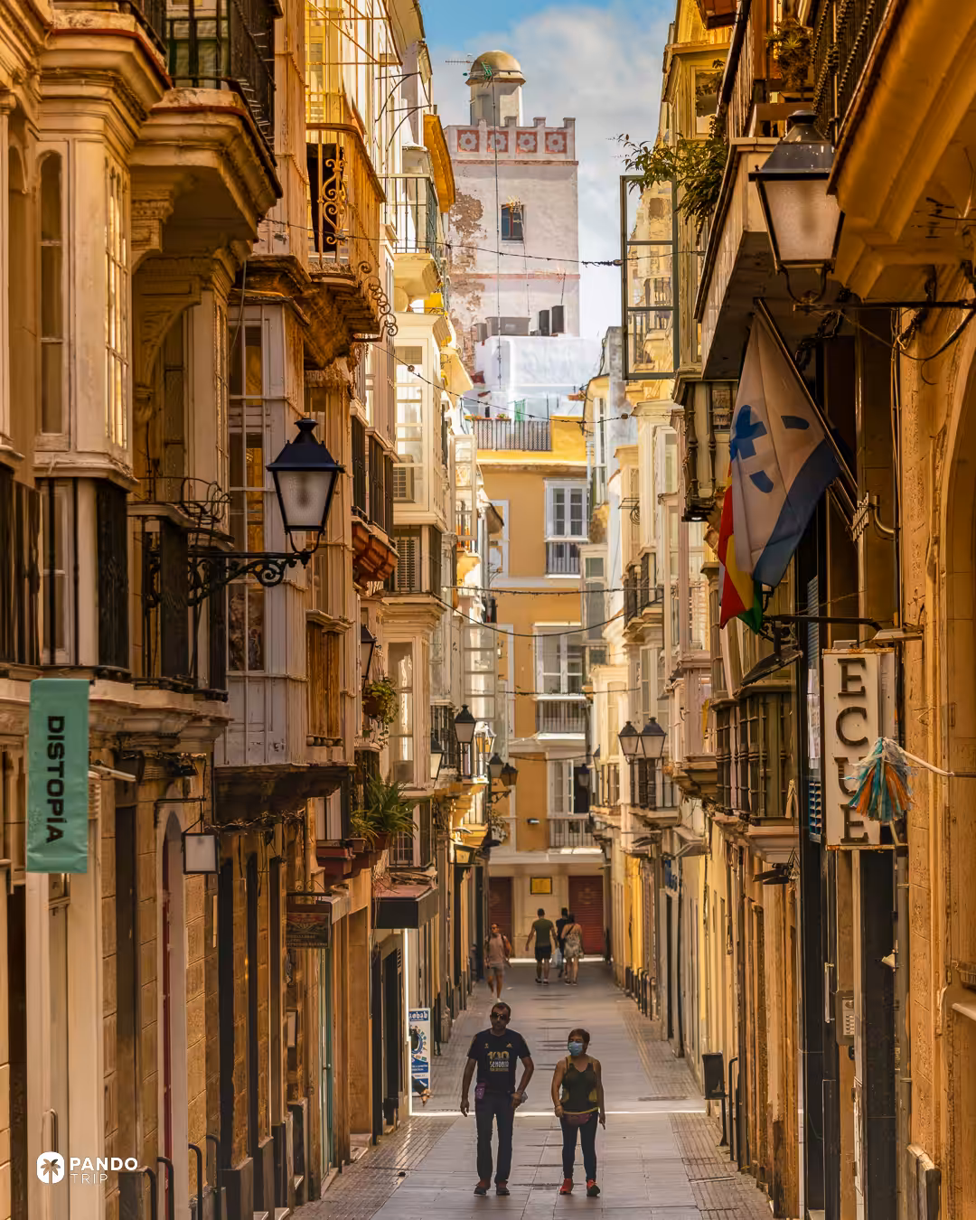 A narrow street of balconied houses in Cadiz with a white lookout tower closing the view at the end.