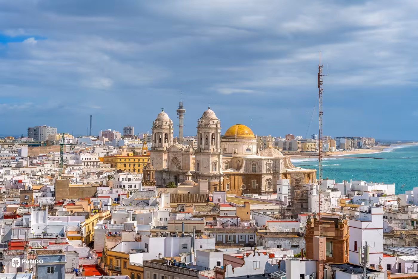 Cadiz from above, the cathedral's golden dome and twin towers over a field of white flat roofs with the Atlantic behind.