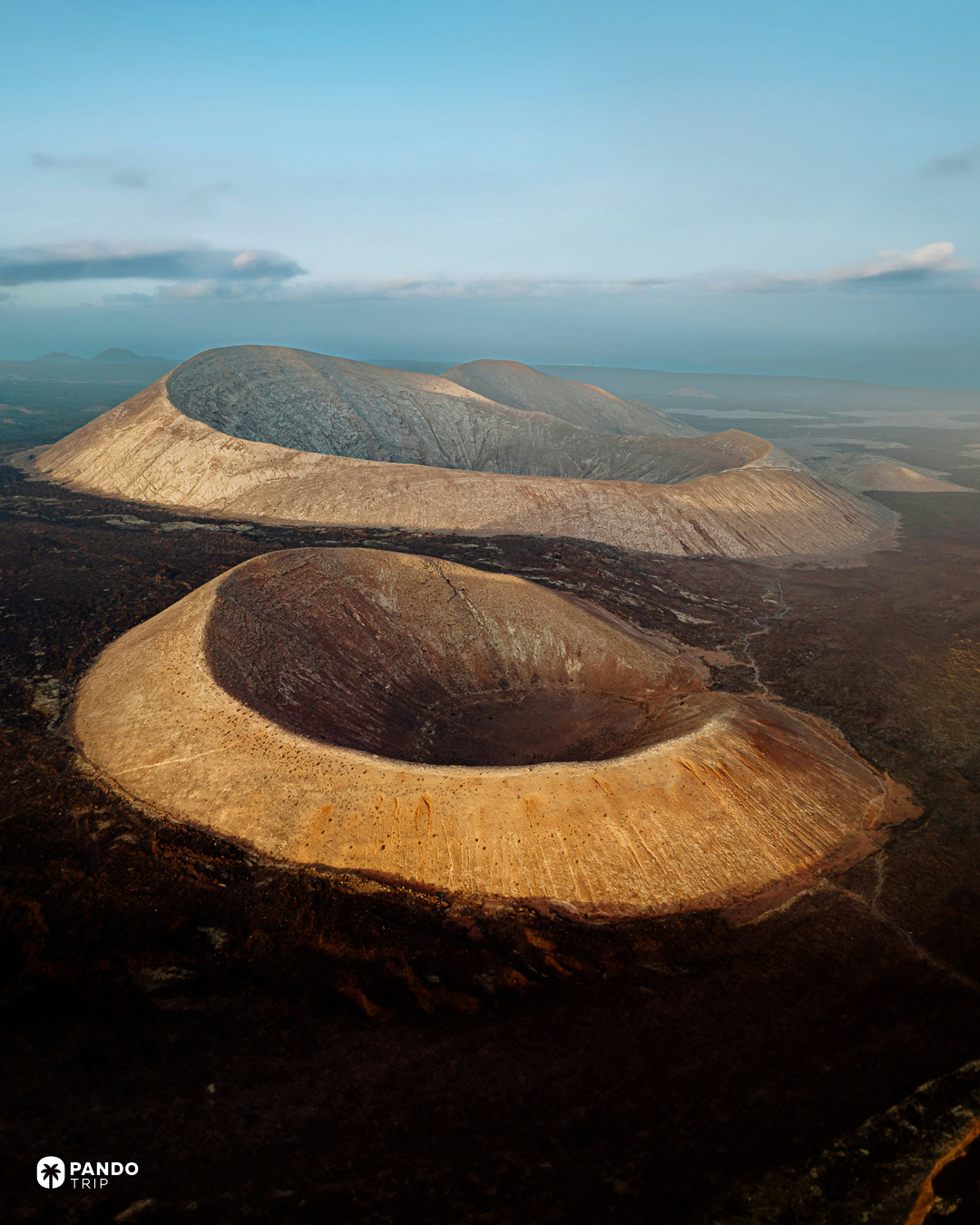 Two volcanic craters rising out of a dark lava field at Caldera Blanca, Lanzarote, seen from the air at low sun.