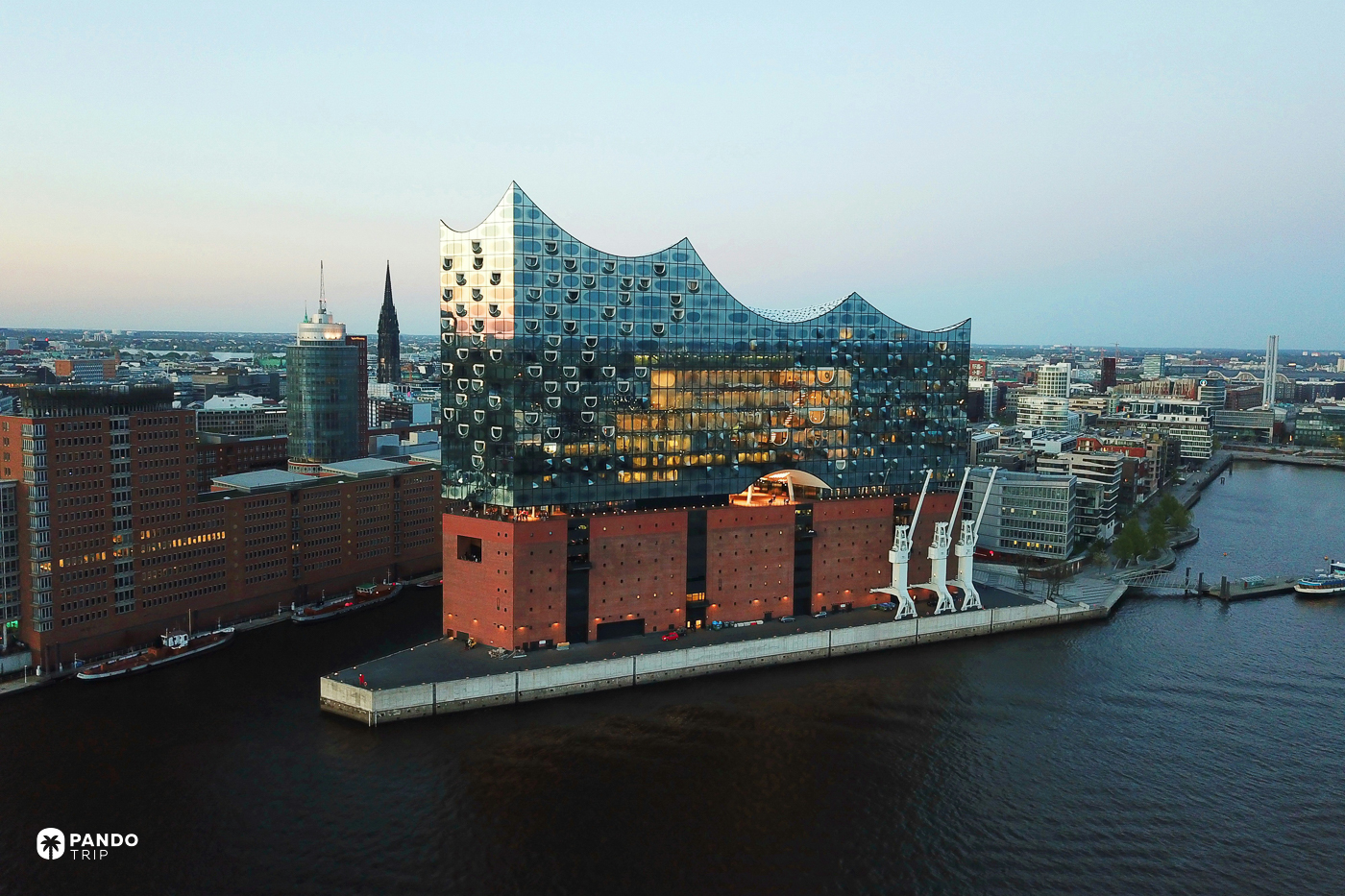 Elbphilharmonie at dusk from the water, the lit glass wave above the red-brick warehouse base.
