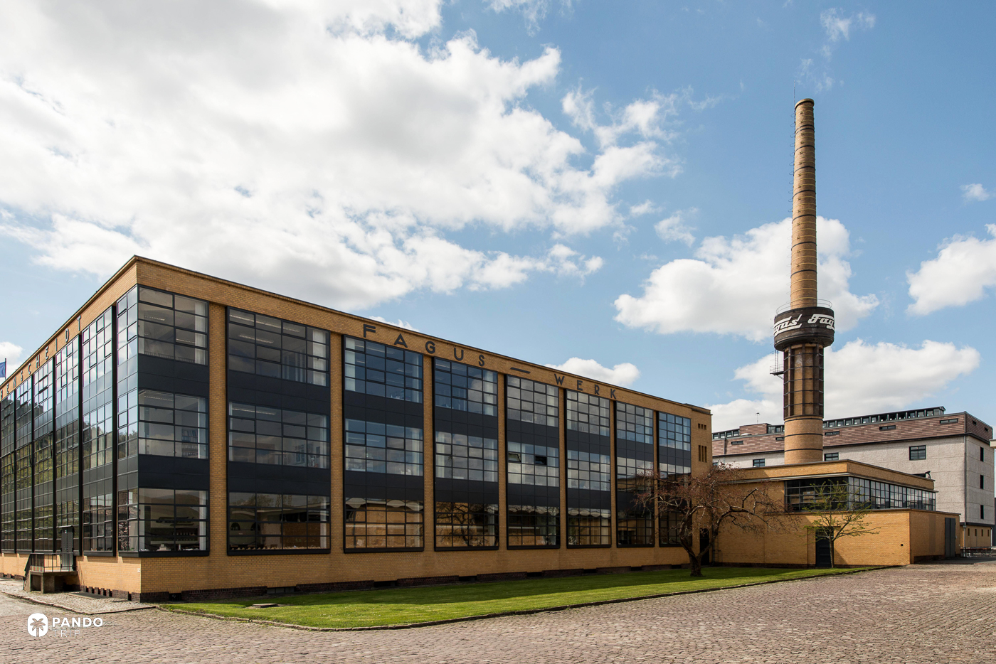 The glazed elevation of the Fagus Factory in Alfeld, with FAGUS WERK lettering and the brick chimney behind it.