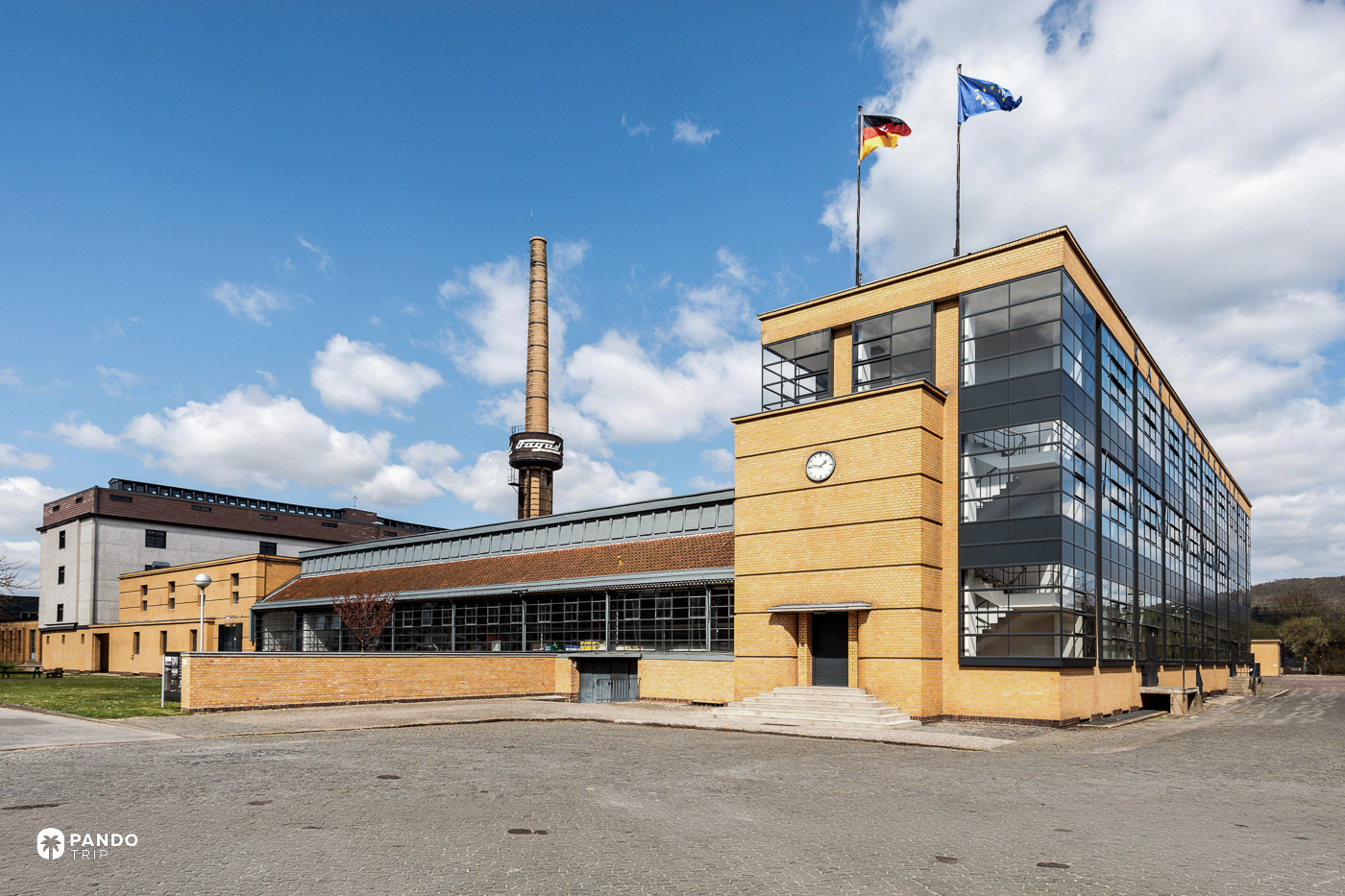The glazed stair block at the Fagus Factory, its brick piers set back behind the glass under German and EU flags.