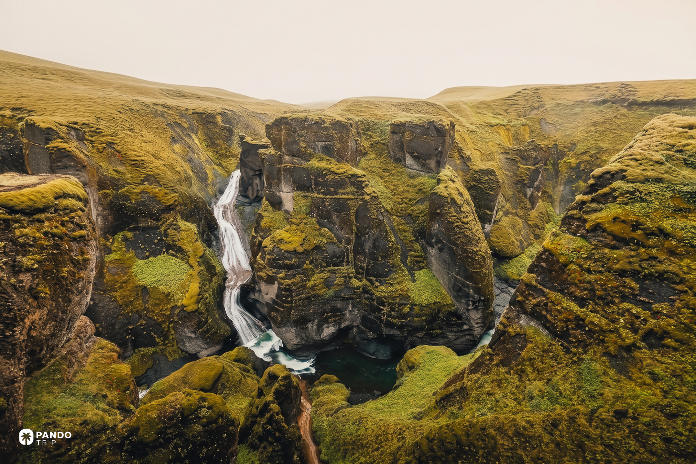 A side stream falling into Fjaðrárgljúfur in a long white ribbon between mossed rock walls.