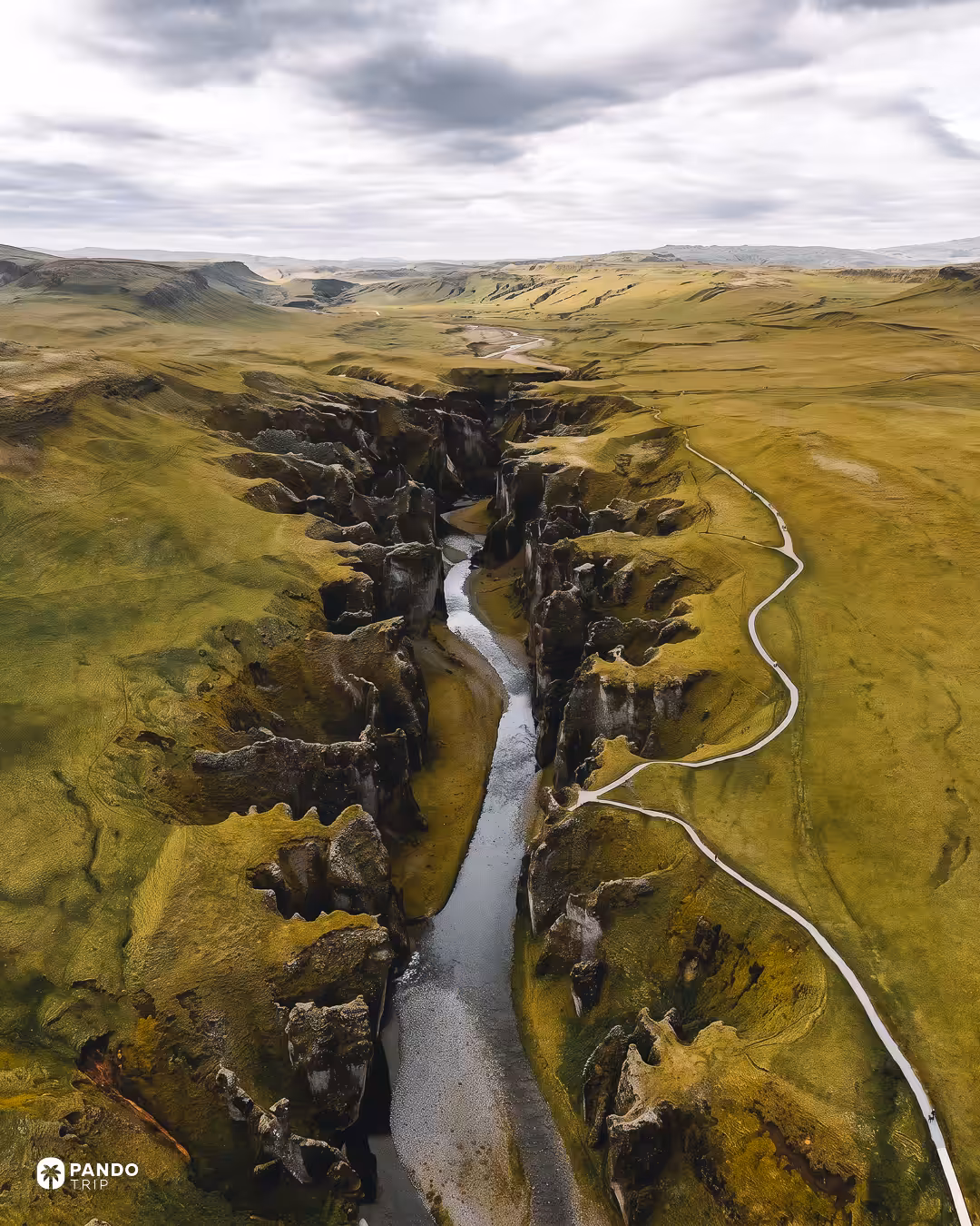 Aerial view of Fjaðrárgljúfur cutting through flat green heath, with the rim footpath running alongside it.