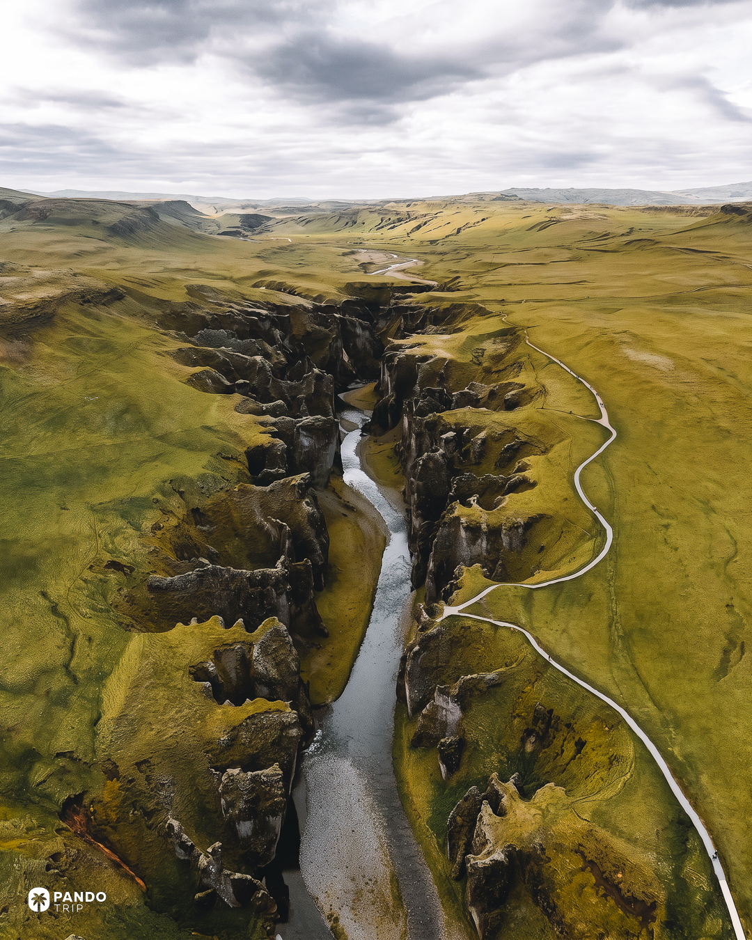 Aerial view of Fjaðrárgljúfur cutting through flat green heath, with the rim footpath running alongside it.