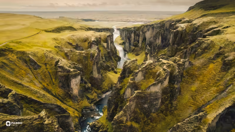 Fjaðrárgljúfur running out toward the flat south Iceland plain, a footpath following the rim.