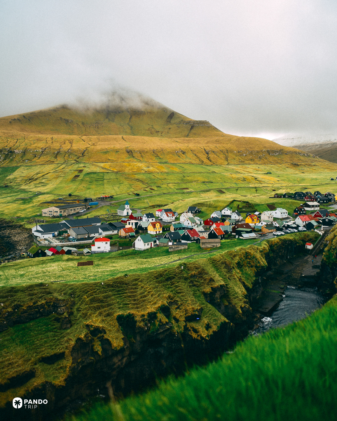 The village of Gjogv in its green valley with cloud sitting on the peak above it, Eysturoy, Faroe Islands.