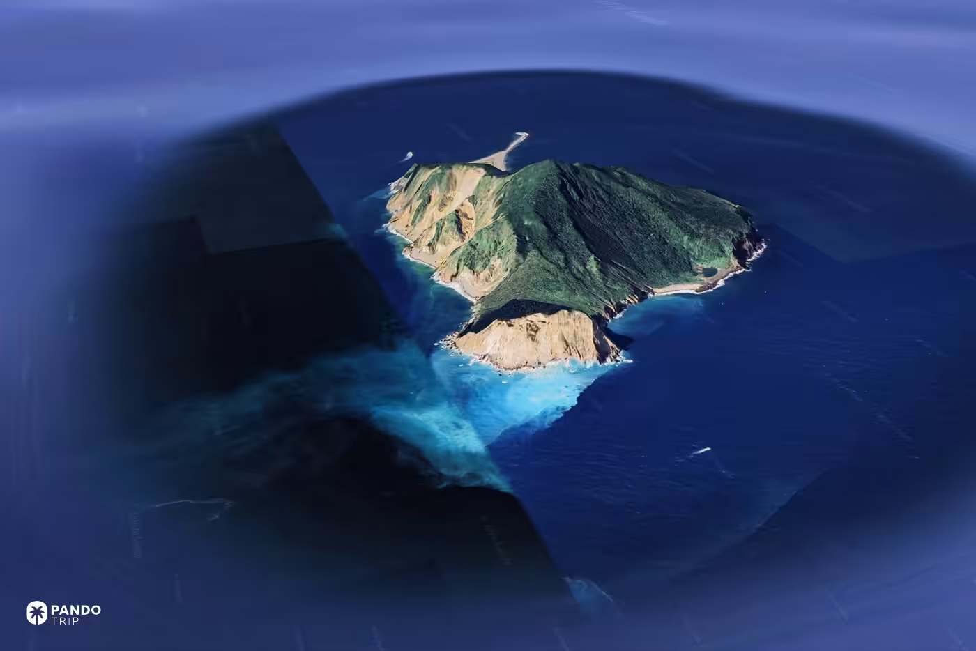 Satellite view of Guishan Island off Taiwan, a pale sulphur plume spreading from its cliffs into dark blue sea.