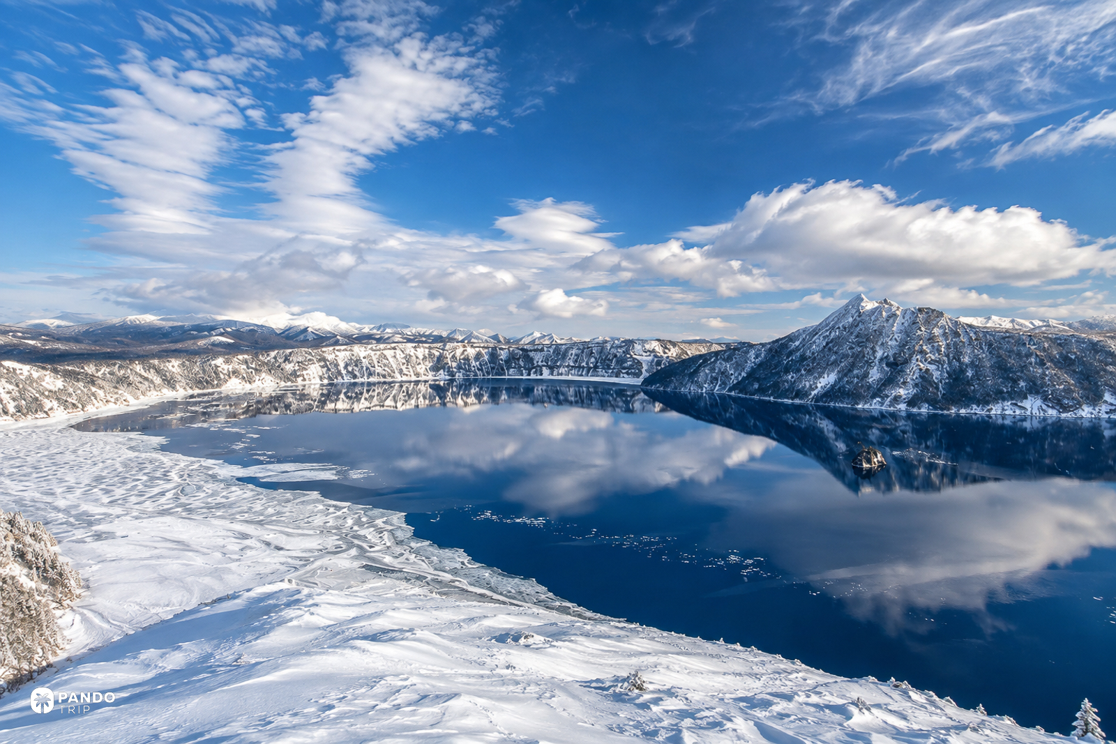 Lake Mashu in winter, the snow-covered caldera rim reflected in dark blue water.